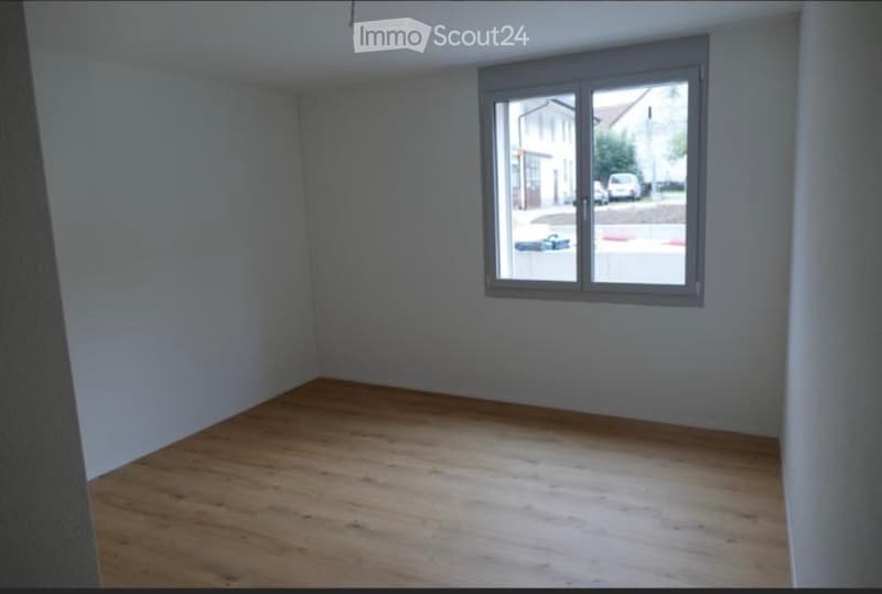 Empty room with wooden flooring and a large window showing a street view.