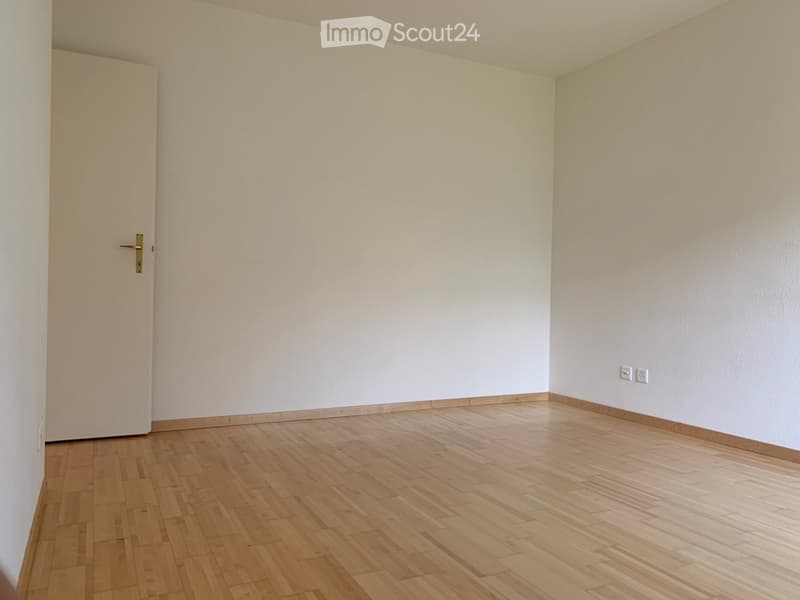 Empty room with light wooden flooring and white walls, featuring a single door and electrical outlets.