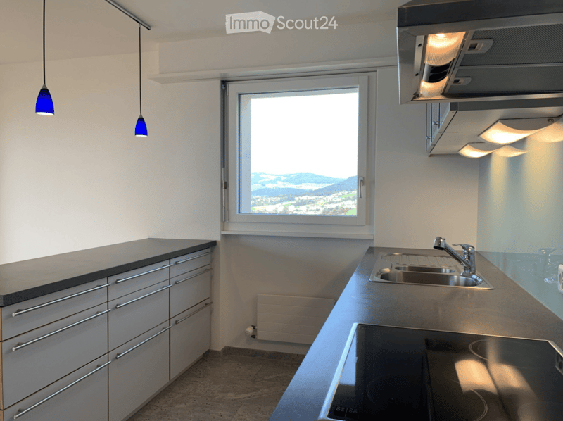 Modern kitchen with stainless steel sink, faucet, stove, and grey cabinets. Large window offers a scenic view.