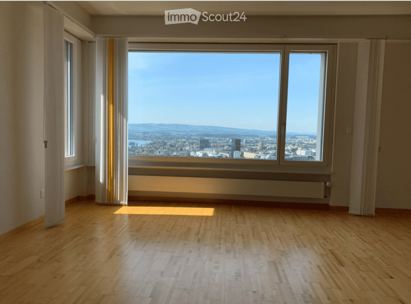 Empty room with wooden flooring, large windows offering a cityscape view, and light-colored walls.
