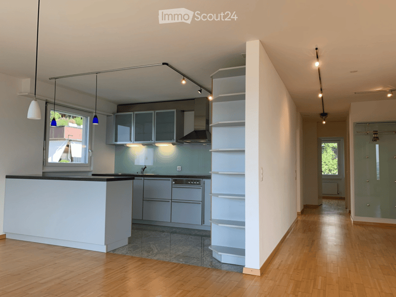 Modern kitchen with light grey cabinets, a central island, and built-in appliances. The space features wooden flooring, pendant lights, and a sleek design with open shelving.