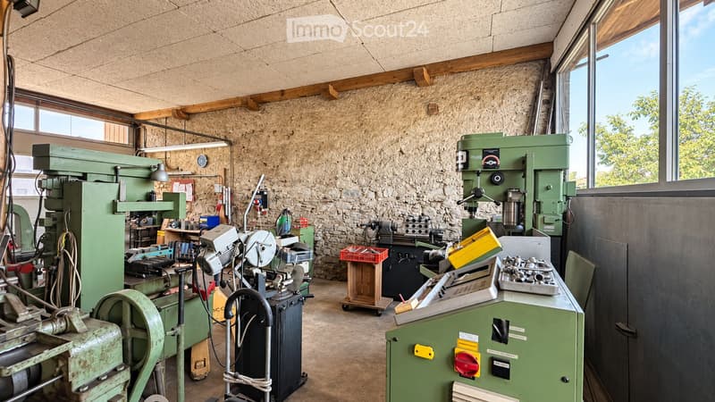 Workshop with stone walls, large windows, and various industrial machines including a drill press, lathe, and workbench.