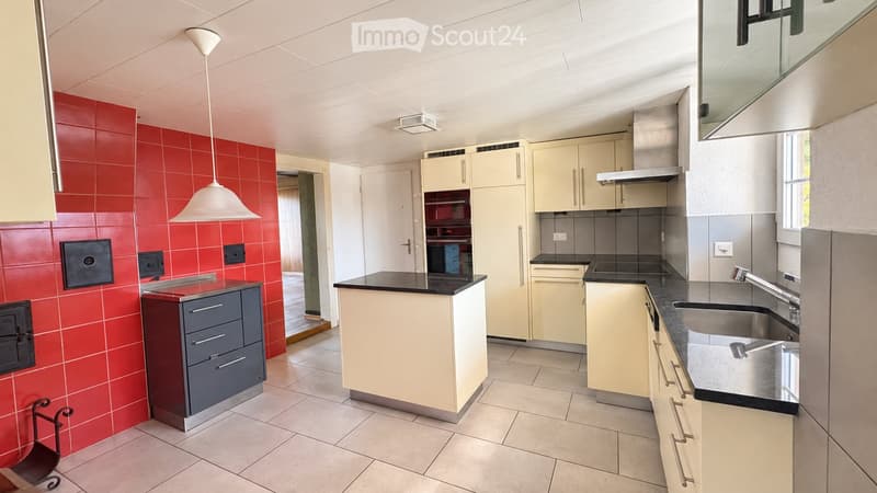 Modern kitchen with light-colored cabinets, black countertops, stainless steel sink, and a red tiled accent wall.