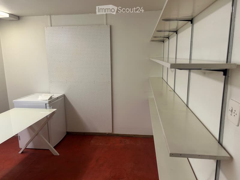 Empty room with white walls, red floor, shelves, and a pegboard wall.