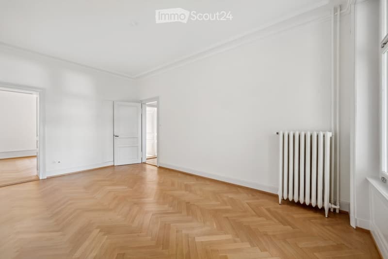 Empty room with white walls, wooden herringbone flooring, and a white radiator on one wall. No furniture or equipment present.