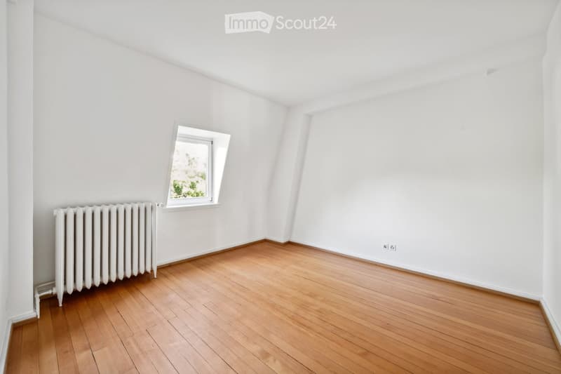 Empty room with wooden flooring, white walls, and a single window with a radiator below it.