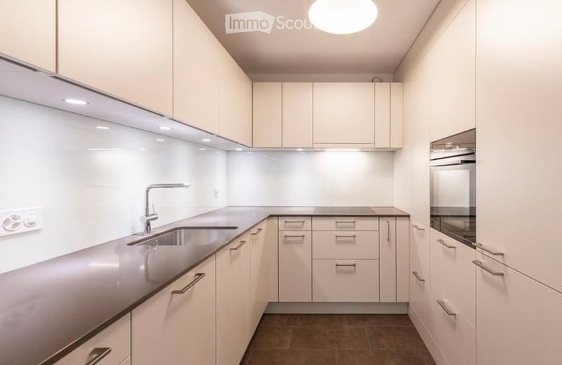 Modern kitchen with white cabinets, stainless steel sink, and built-in oven. Features sleek countertops and integrated lighting.