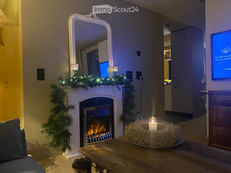 Cozy living room with a fireplace, sofa, coffee table, mirror, and television. Decorated with festive garlands and a candle on the coffee table.