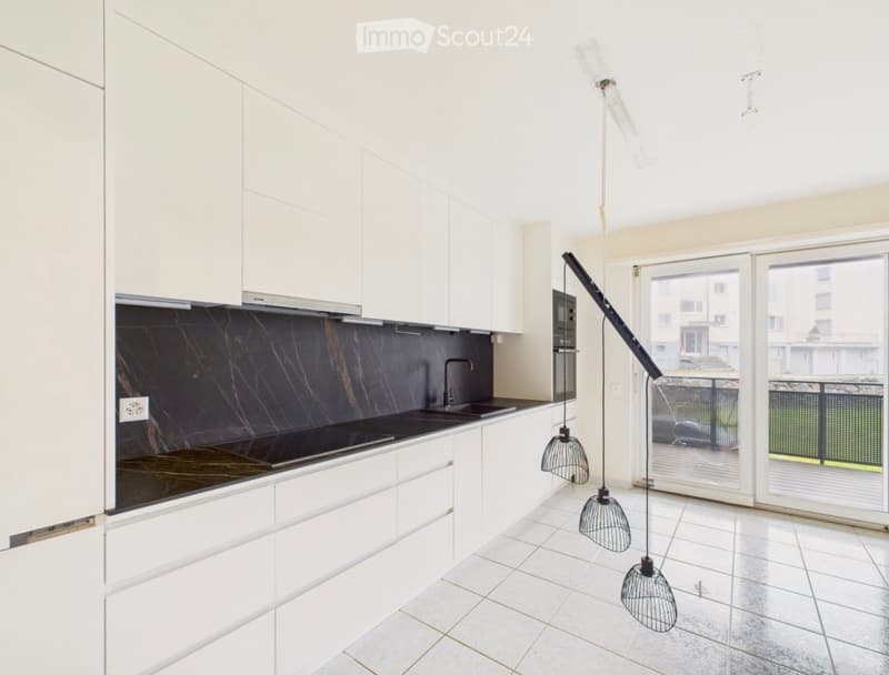 Modern kitchen with white cabinets, dark marble backsplash, and pendant lights. Features a sink, oven, and large windows with a view of the balcony.