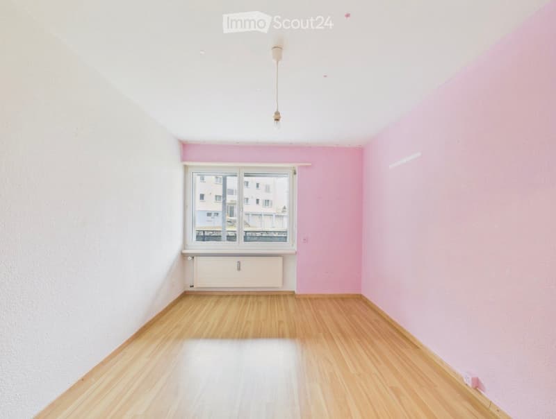 Empty room with light pink and white walls, wooden flooring, a single window with white frame, and a radiator below the window.