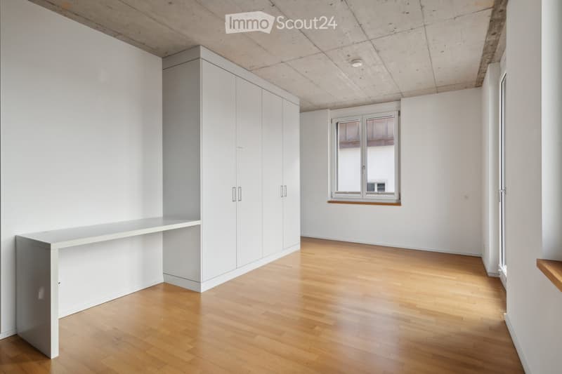 Empty room with light wooden flooring, white walls, built-in cabinetry, and a window with a view of another room.