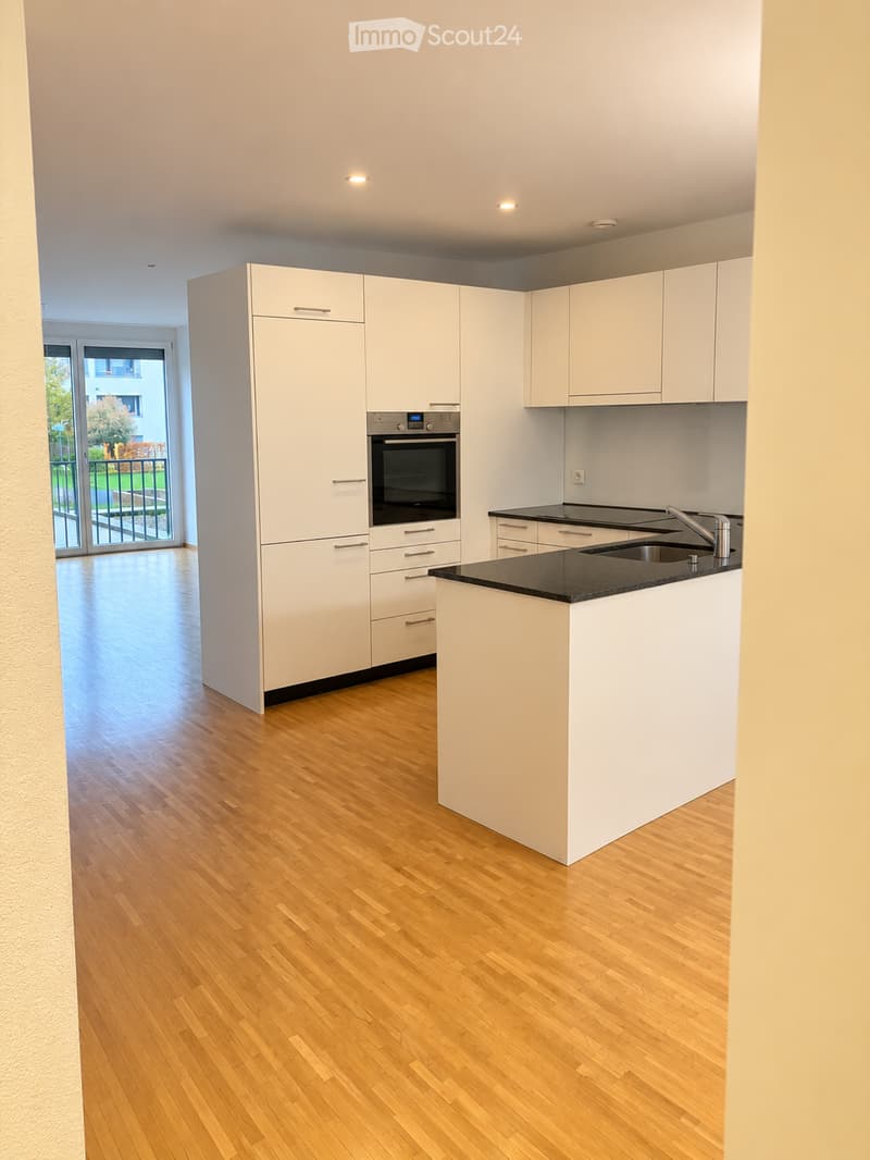 Modern kitchen with white cabinets, a central island, and a black countertop. Features include a sink with a modern faucet, an oven, and a sliding glass door leading to a balcony.