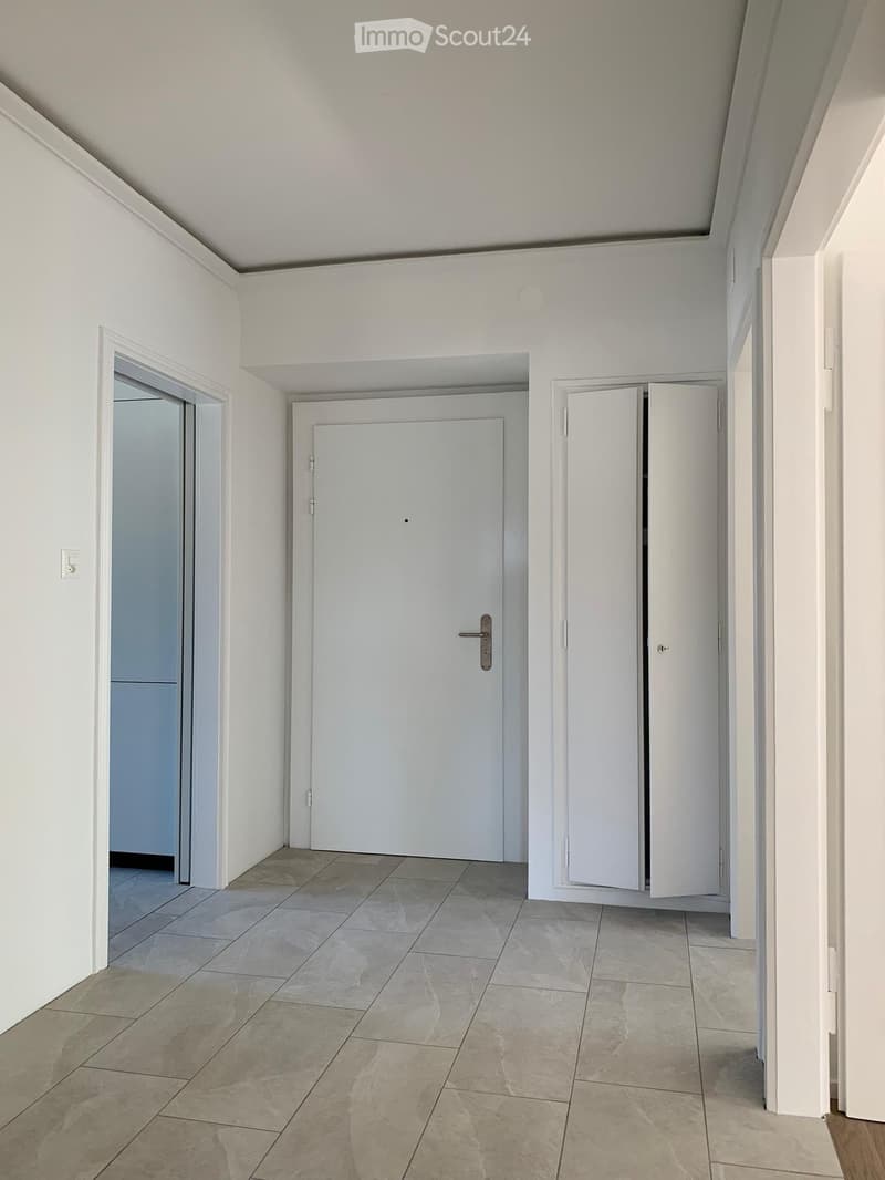 Empty hallway with white walls, tiled floor, and several doors including a closet and an open doorway.