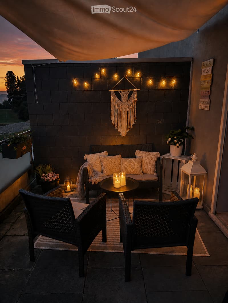 Cozy balcony with a sofa, small round table, two wicker chairs, candles, a lantern, and a decorative hanging ornament.