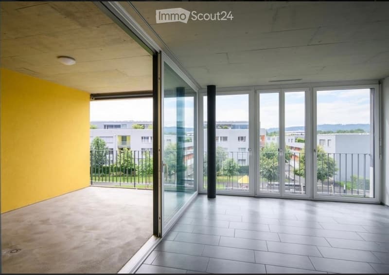 Empty balcony with large glass doors, tiled floor, yellow wall, and metal railing overlooking a residential area.