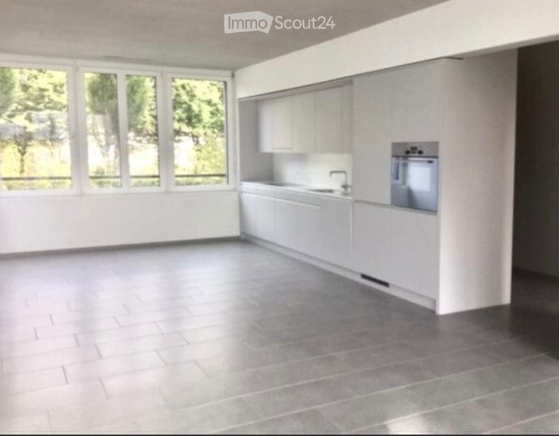 Empty kitchen with white cabinets, a sink, and a built-in oven. Large windows provide natural light.