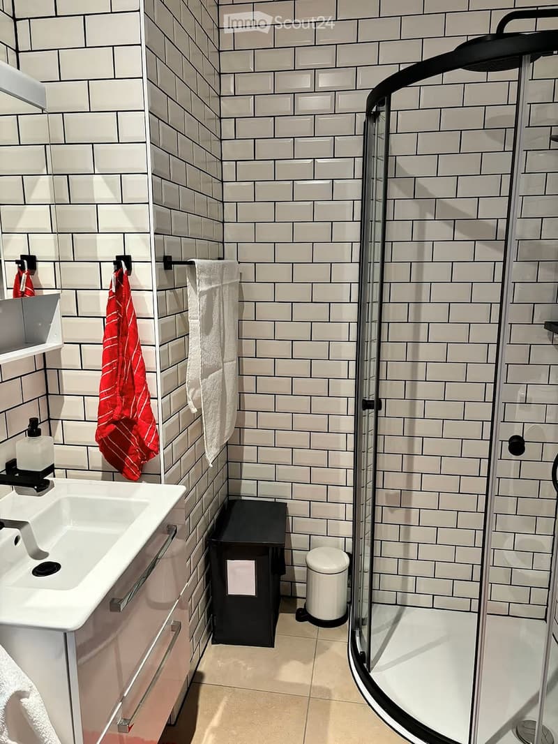 Modern bathroom with white tiles, a glass-enclosed shower, a white sink with a mirror, and towels hanging on a rack.