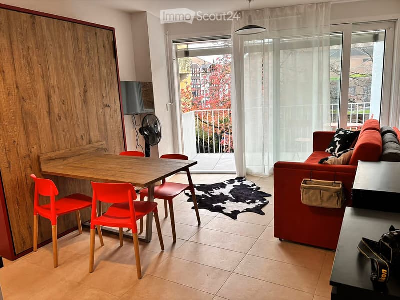 Modern living room with a red sofa, wooden dining table, red chairs, and a fan near the balcony.