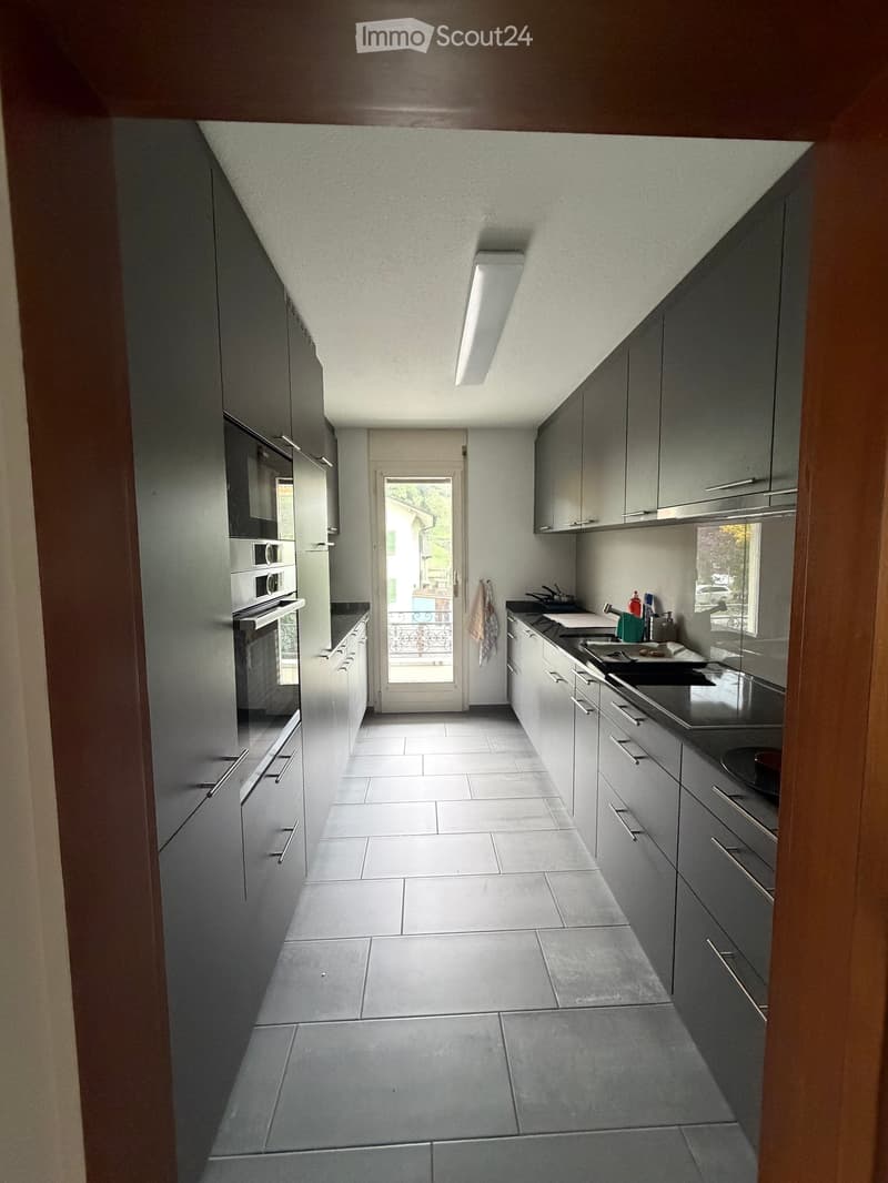 Modern kitchen with grey cabinets, white tiled floor, and stainless steel appliances including an oven and sink.