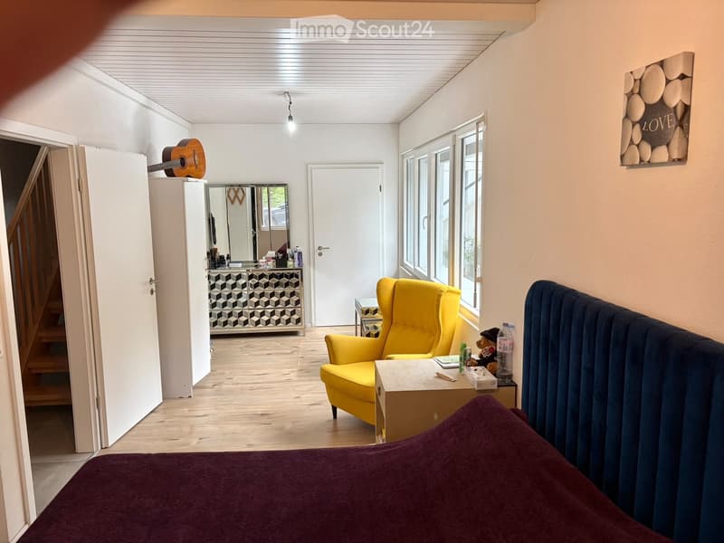 A cozy living space with a yellow armchair, a blue sofa, a small table with various items, a guitar on top of a cabinet, and a mirror in the background.