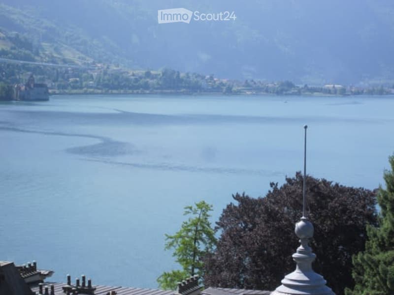 View from a balcony or terrace overlooking a large lake with distant hills and a town on the far shore.