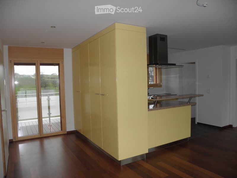 Modern kitchen with light yellow cabinets, a range hood, and a countertop. The space features wooden flooring and a sliding glass door leading to a balcony.