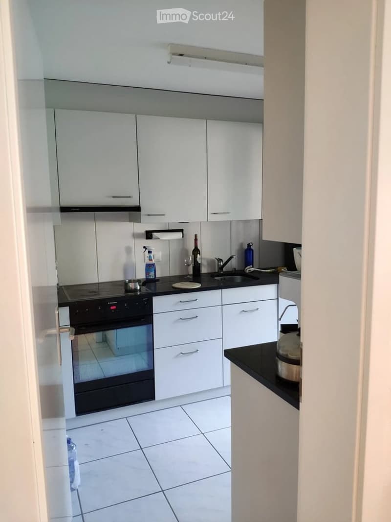 Modern kitchen with white cabinets, black countertops, and stainless steel appliances. Features an oven, sink, and various bottles and cups on the counter.