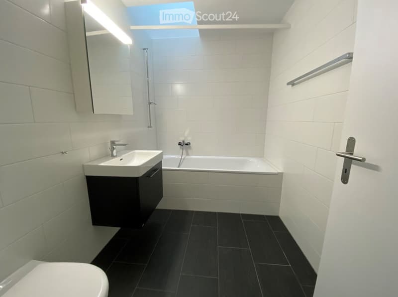 Modern bathroom with white tiles, black floor, sink, bathtub, toilet, and mirror.