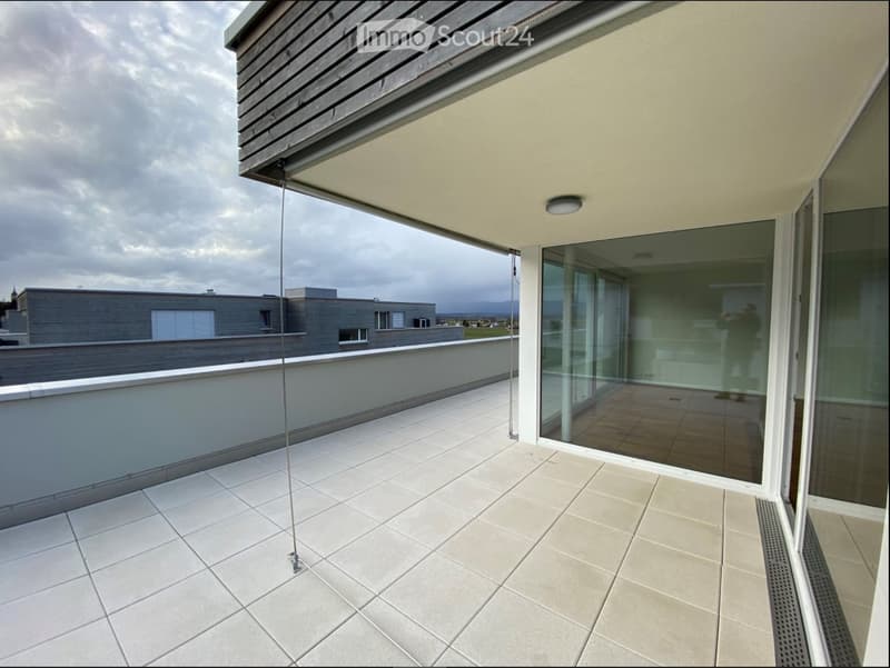 Modern balcony with tiled flooring, glass railing, and a view of the surrounding area.