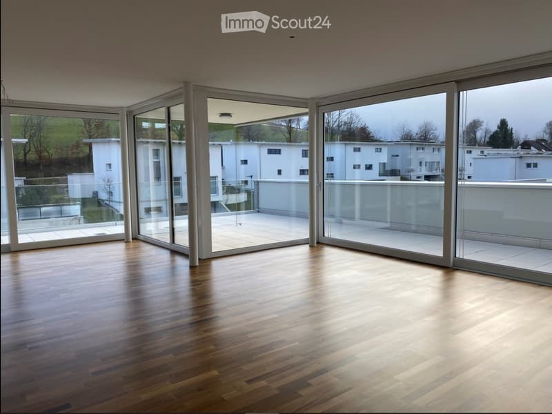 Empty room with wooden flooring and large sliding glass doors leading to a balcony or terrace. The room is well-lit with natural light and has a modern, minimalist design.