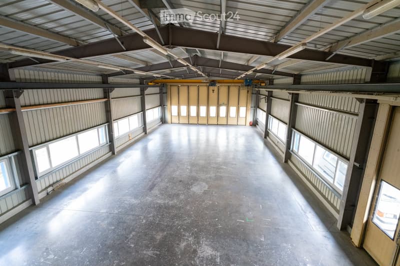Empty warehouse space with concrete floor, metal walls, large windows, and overhead doors.