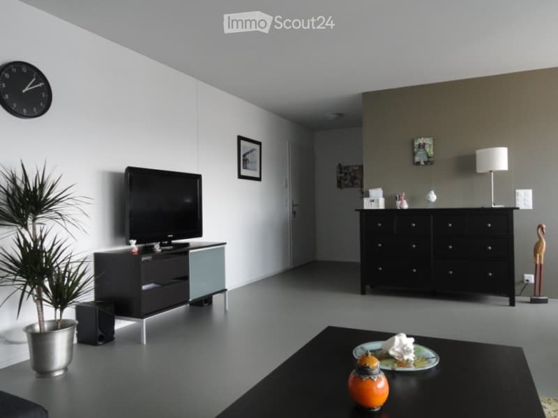 Modern living room with a sleek black TV stand, a coffee table with decorative items, a potted plant, a black cabinet with a lamp, and a wall-mounted clock.
