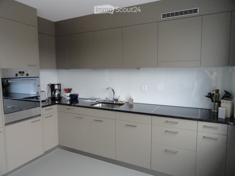 Modern kitchen with grey upper cabinets, white lower cabinets, black countertops, and stainless steel appliances. Includes a sink, faucet, oven, coffee maker, and various small items on the counter.