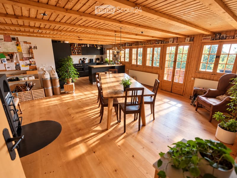 Bright, open-plan living and dining area with wooden floors, exposed wooden beams, large windows, a dining table with chairs, a sofa, and a kitchen area with cabinets and appliances.