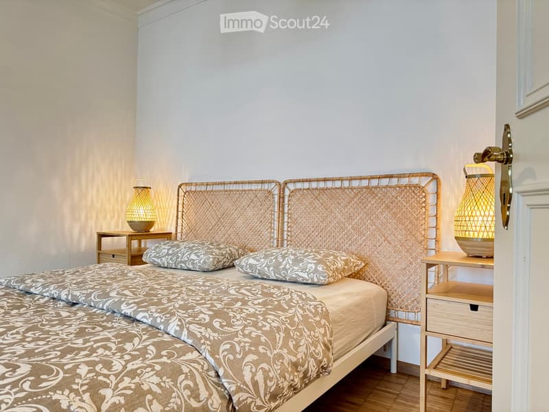 Cozy bedroom with a double bed, woven headboard, patterned bedding, two nightstands with lamps, and wooden flooring.