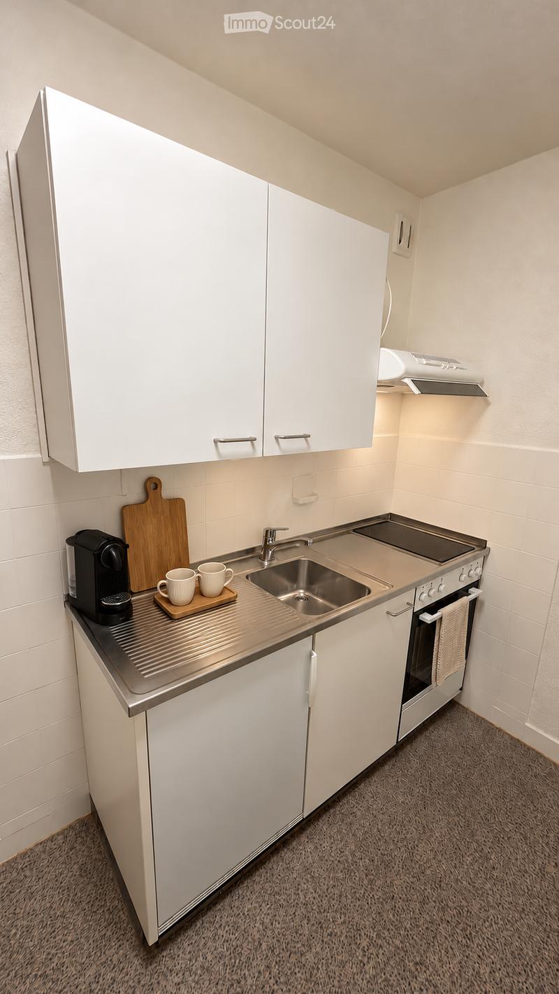 Compact kitchen with white cabinets, stainless steel sink, coffee maker, cutting board, and cups on the counter.
