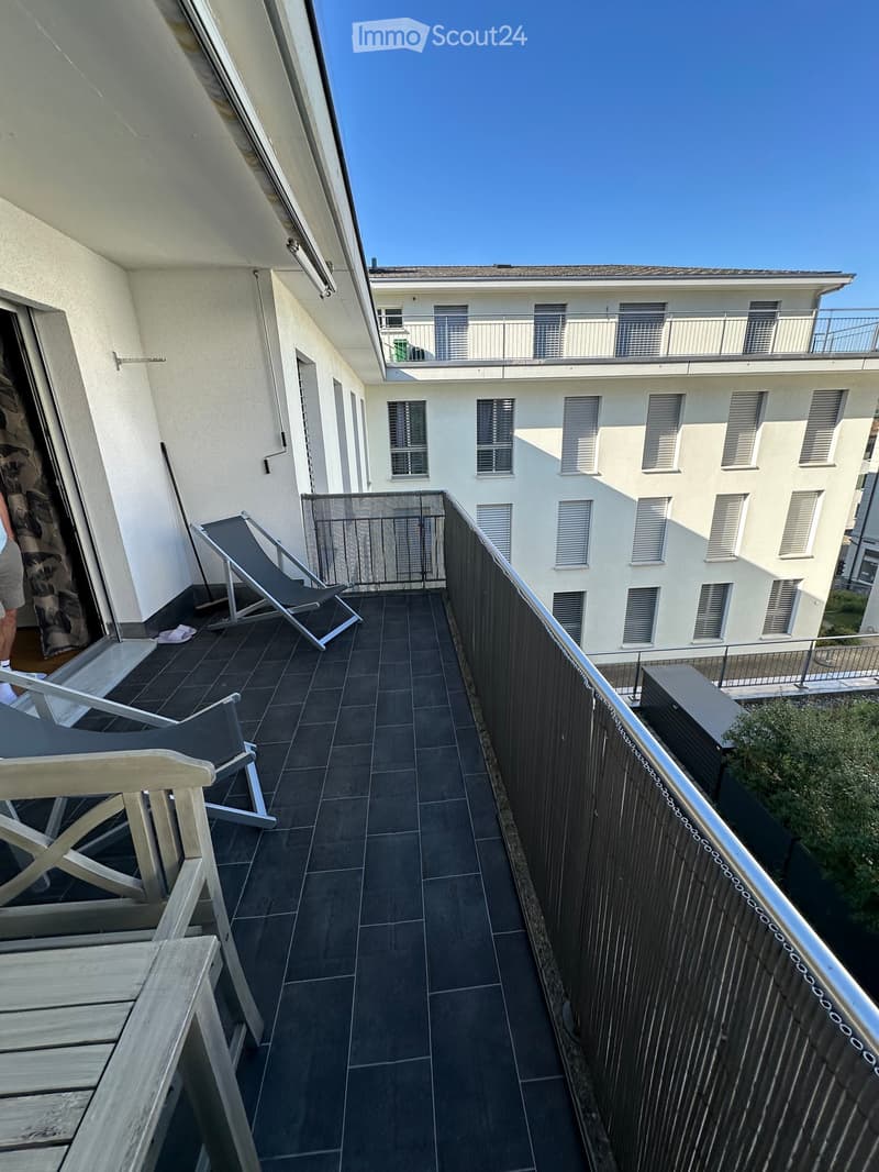 Balcony with dark tiled floor, metal railing, and two lounge chairs.