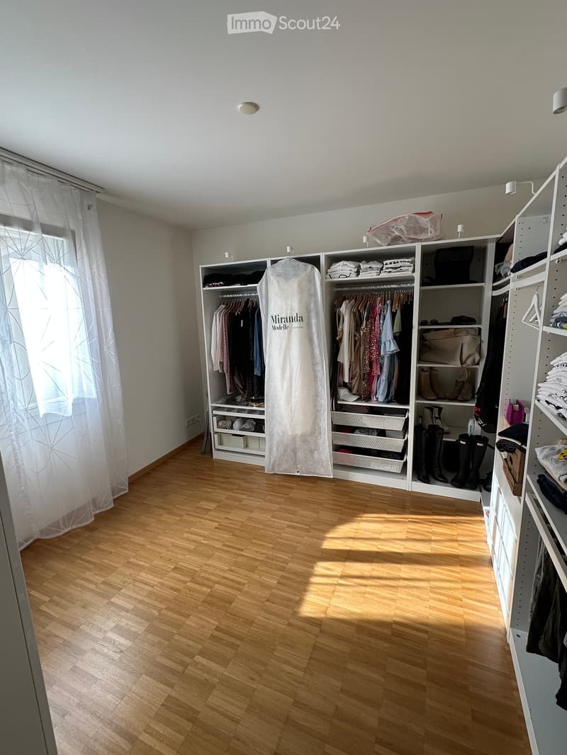 Empty room with wooden flooring, large built-in wardrobe with multiple sections, and a window with white curtains.