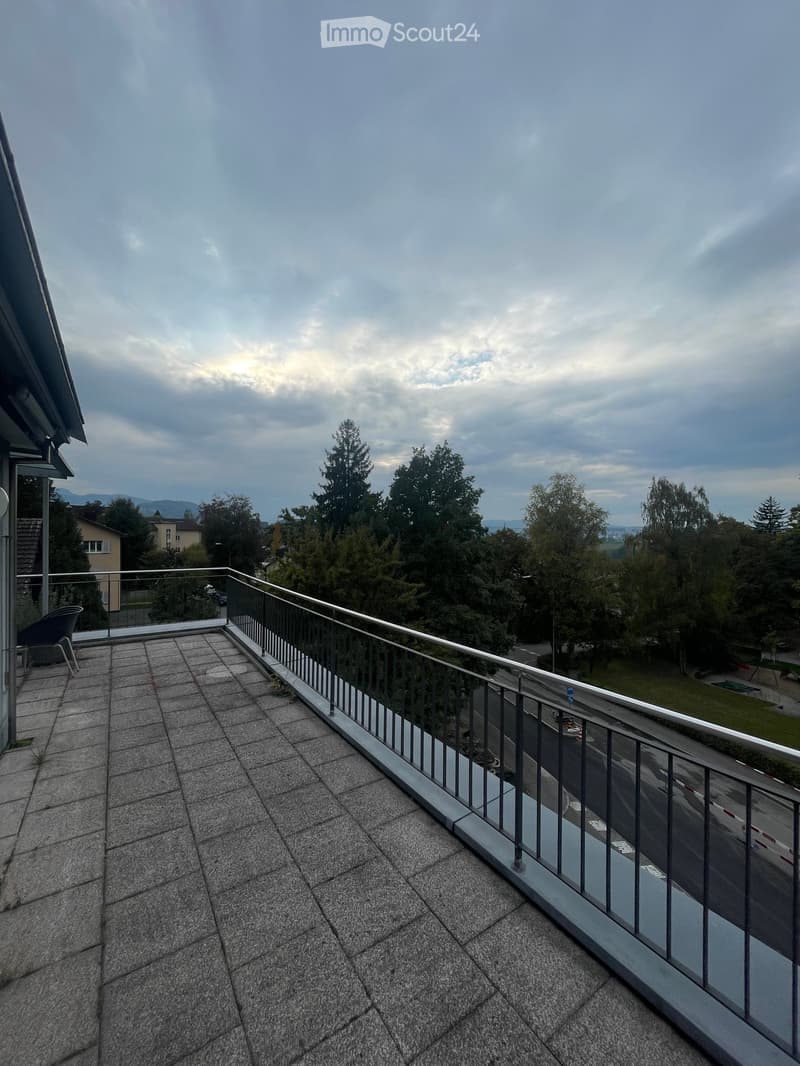 Balcony with tiled floor, metal railing, and a view of trees and a road.