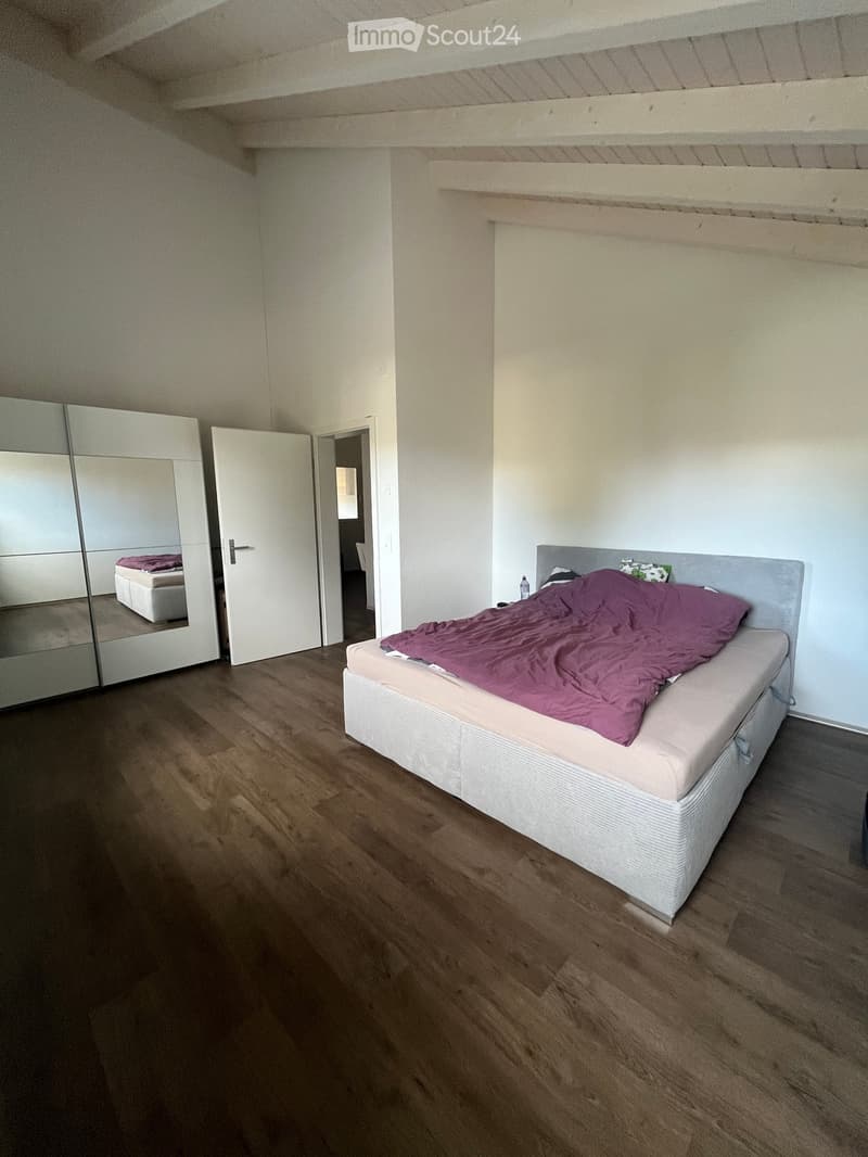 Modern bedroom with wooden flooring, a single bed with a purple duvet, a large mirror, and a wardrobe.