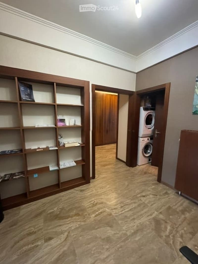 Empty room with wooden shelving unit, light-colored carpet, and a private washing machine in an adjacent closet.