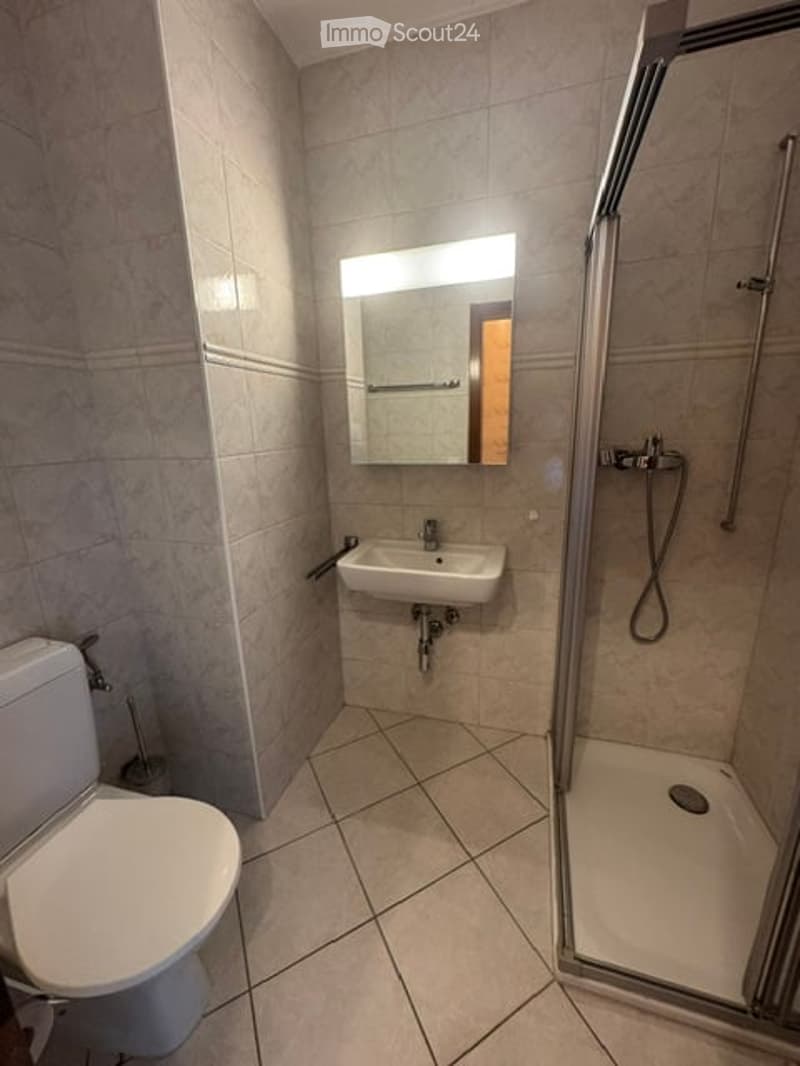 Modern bathroom with beige tiled walls and floor, a white toilet, a sink with a mirror above it, and a glass-enclosed shower with a handheld showerhead.