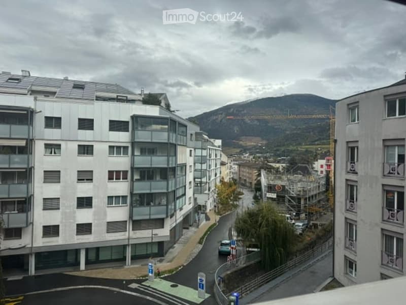 Modern apartment buildings with large windows and balconies overlooking a city street and distant mountains.