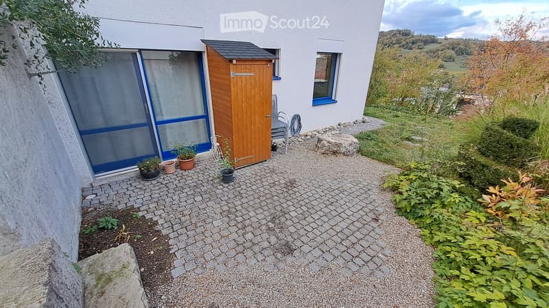 Garden area with a paved pathway, small wooden shed, potted plants, and a view of the surrounding landscape.