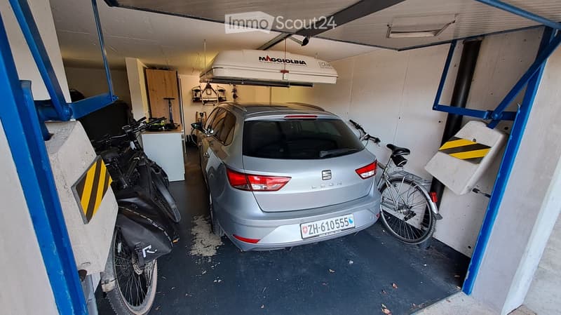 Garage with a parked car, two bicycles, and a storage box on the ceiling.