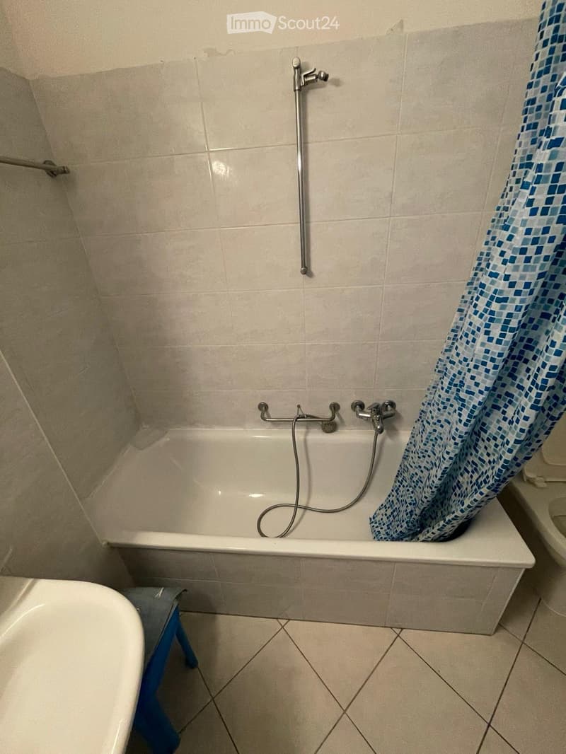 Bathroom with a bathtub, shower curtain, and a small blue stool next to the tub.