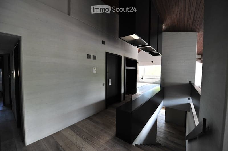 Modern hallway with wooden flooring, white walls, black doors, and a sleek black railing leading to an open area with natural light.