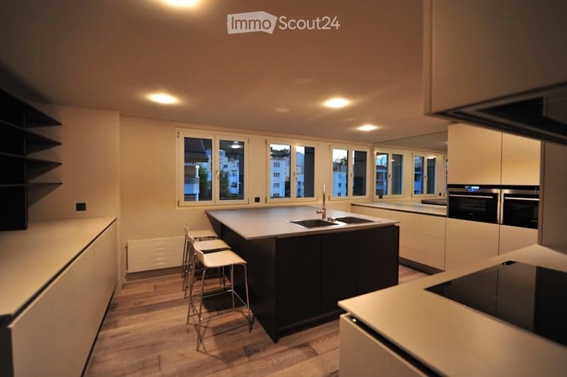 Modern kitchen with white cabinets, dark kitchen island, stainless steel appliances, and bar stools.