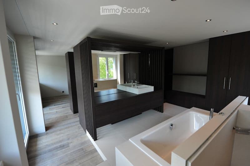 Modern bathroom with dark wood cabinets, white sink, bathtub, and large mirror. The space features recessed lighting and a sleek design.