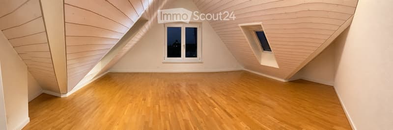 Empty attic room with wooden flooring, slanted wooden ceiling, and large window with a view.